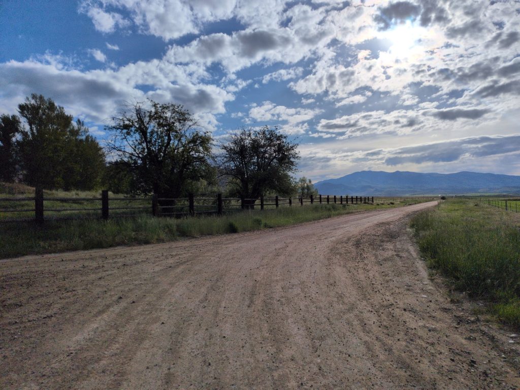 Y-junction near Aid Station 2 with cottonwoods, a metal cattle gate, and mountains in the distance.